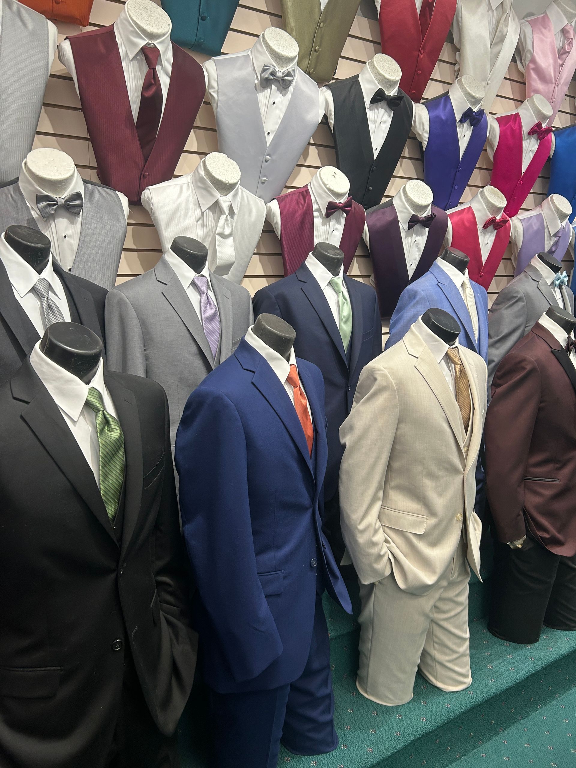 Mannequins in suits and formalwear arranged in a storefront display, in various colors and styles.