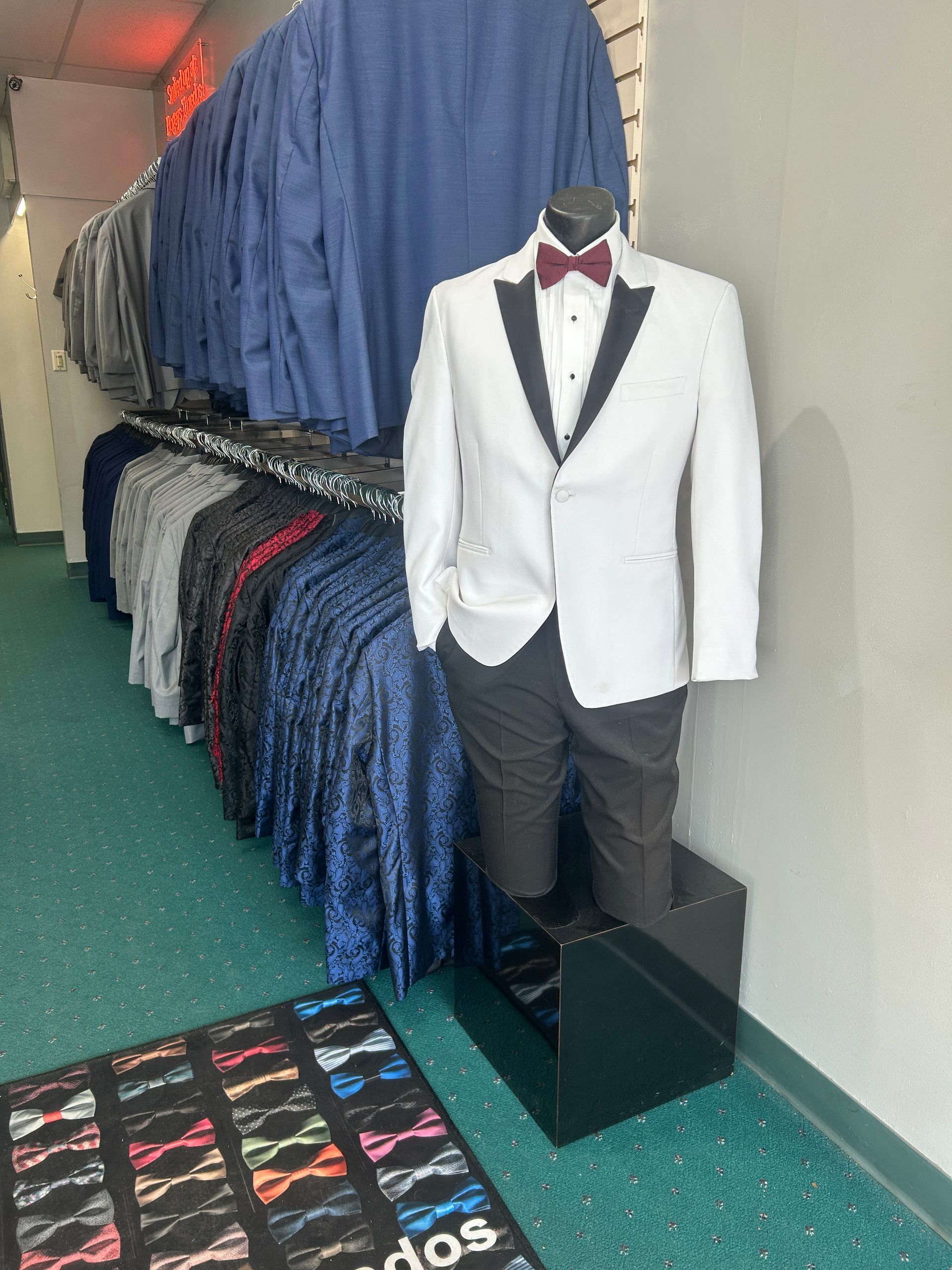 White tuxedo jacket on a mannequin in a clothing store aisle, with rows of suits behind it.