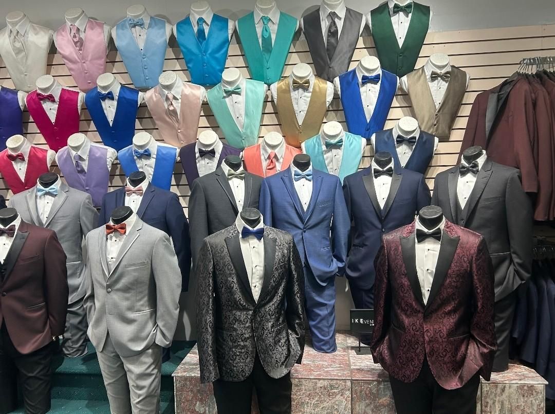 Mannequins in a shop window display formal suits and blazers in assorted colors.