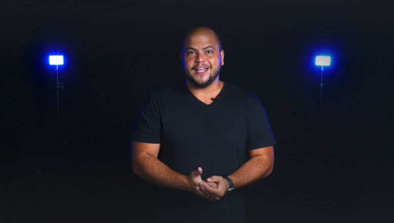 Um homem de camisa preta está parado em frente a duas luzes em um quarto escuro.