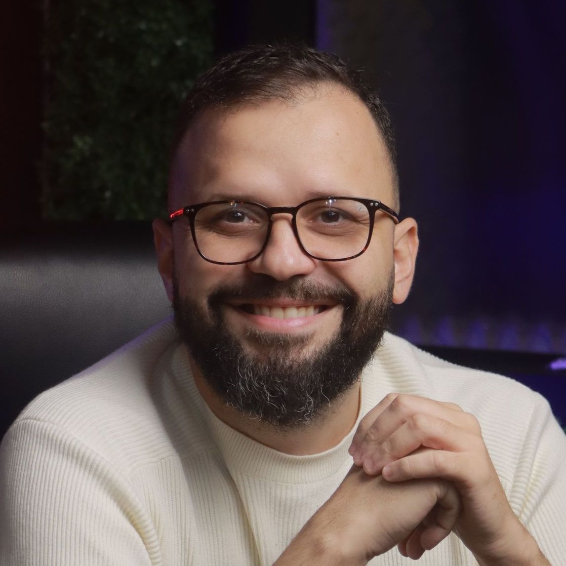 Um homem com barba e óculos está sorrindo para a câmera.