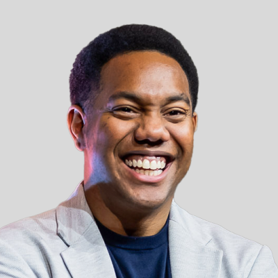 Um homem vestindo uma jaqueta e uma camisa azul está sorrindo.