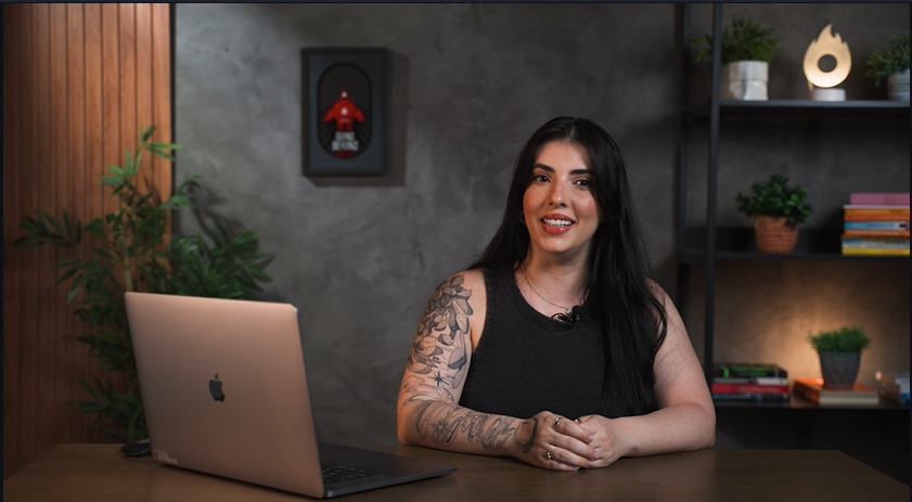 Uma mulher está sentada em uma mesa em frente a um laptop.