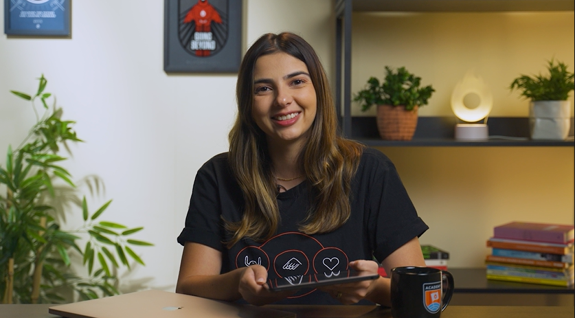 Uma mulher está sentada em uma mesa segurando um tablet e sorrindo.