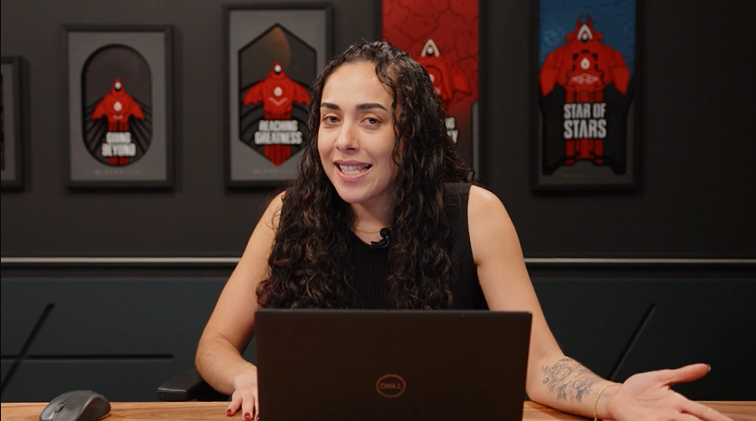 Uma mulher está sentada em uma mesa em frente a um laptop.