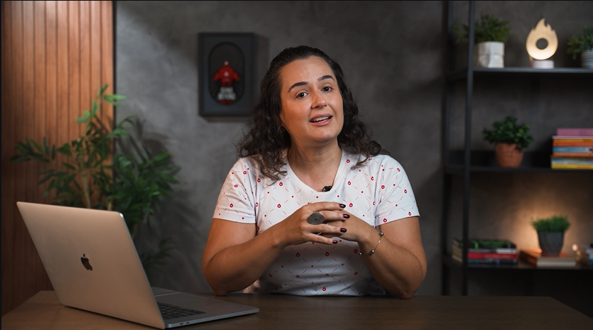 Uma mulher está sentada em uma mesa em frente a um laptop.