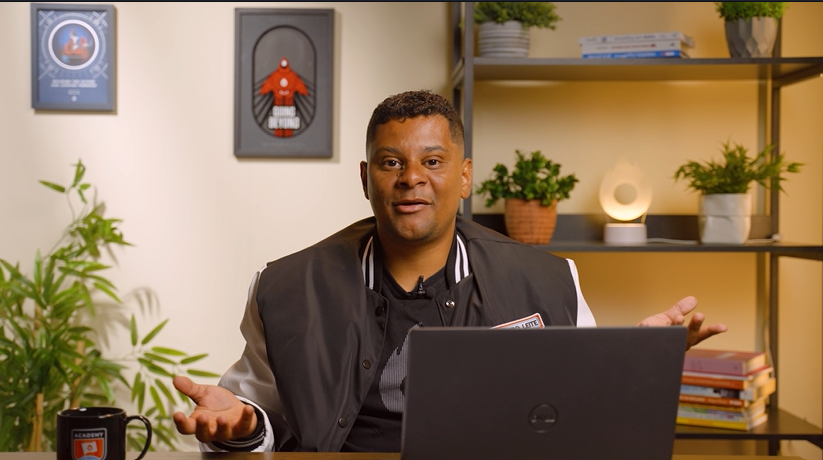 Um homem está sentado em uma mesa em frente a um laptop.
