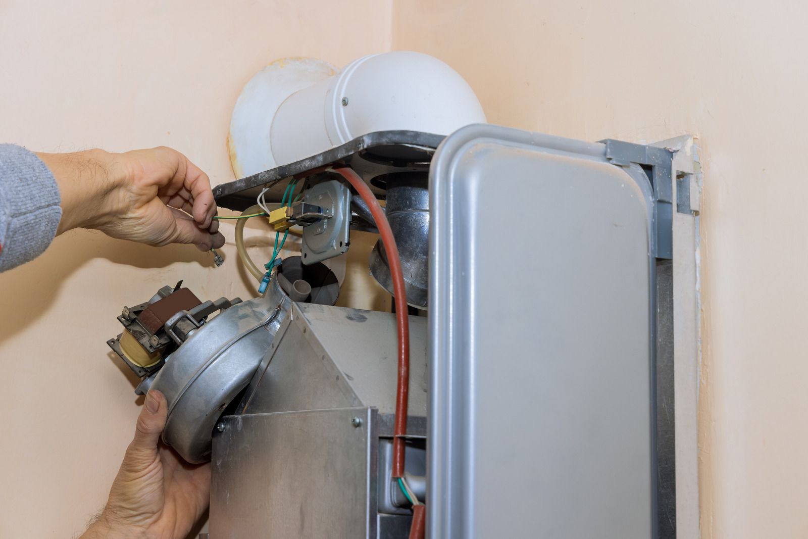A man is fixing a boiler with a screwdriver.