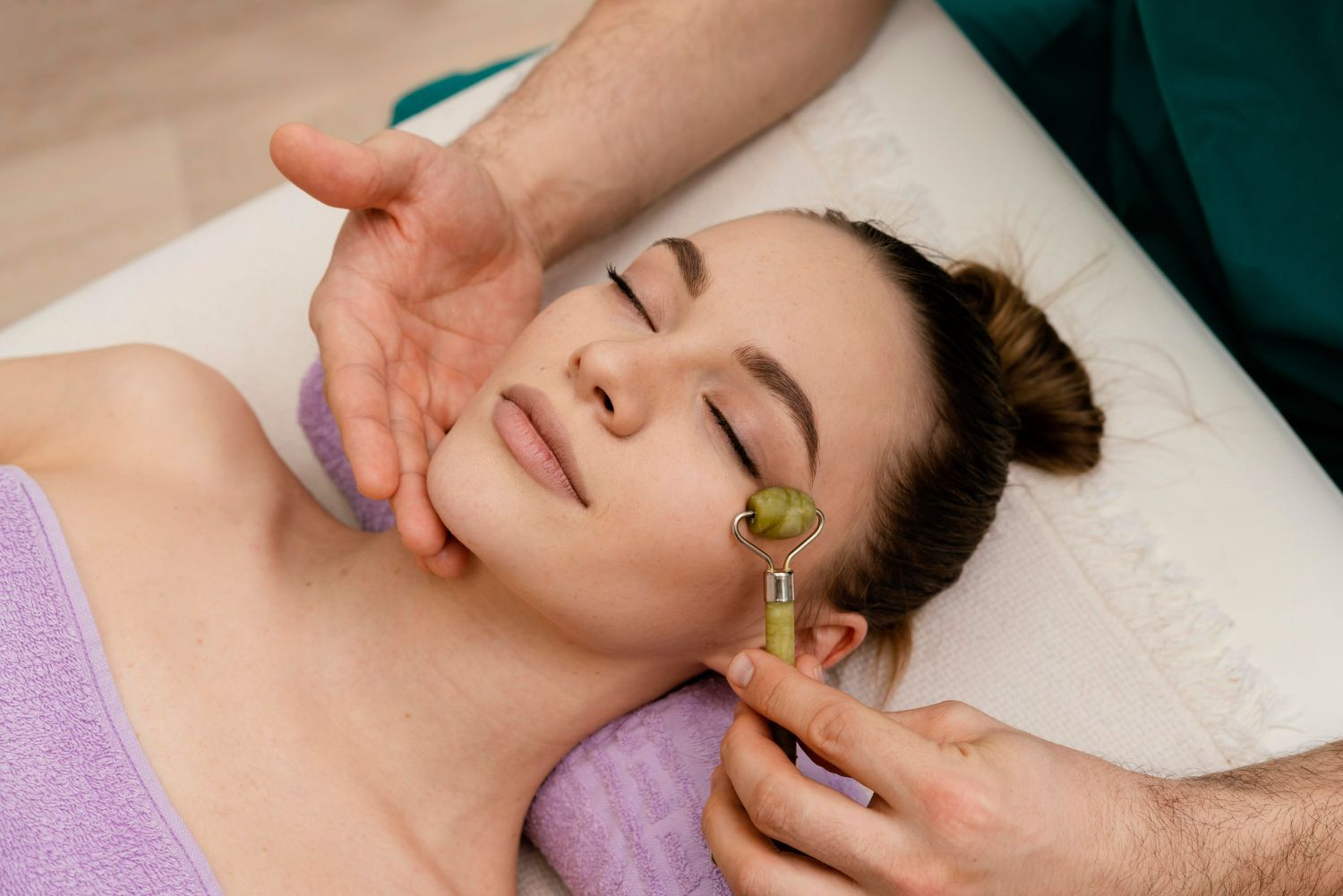 A woman is getting a facial massage with a jade roller.