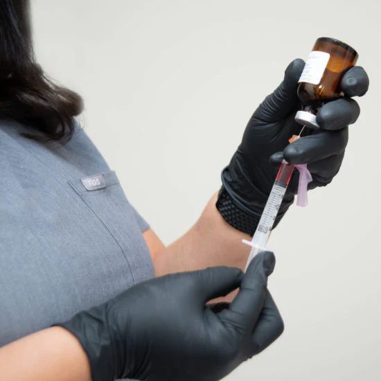 A woman wearing black gloves is holding a syringe and a bottle