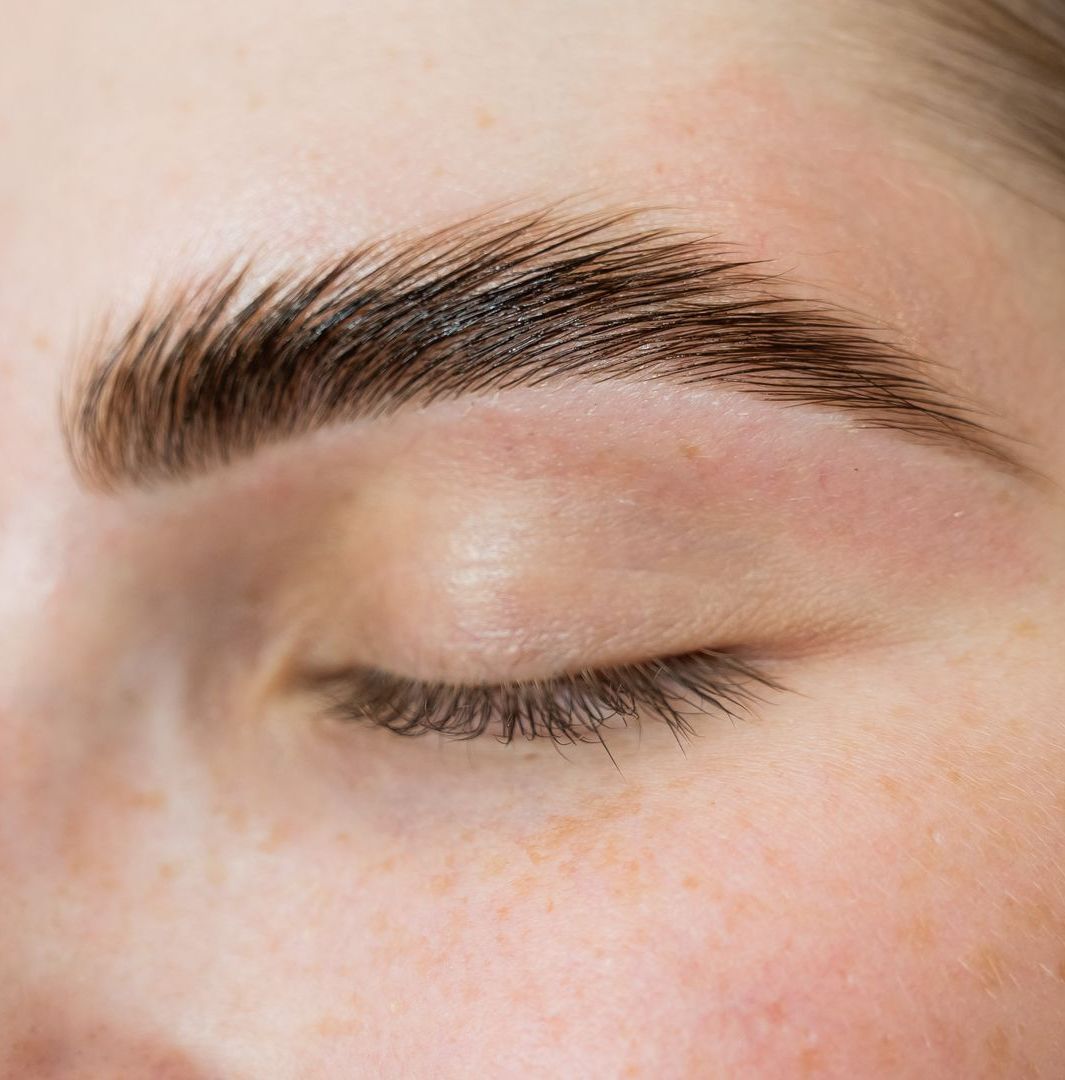 A woman is getting her eyebrows painted by a makeup artist.