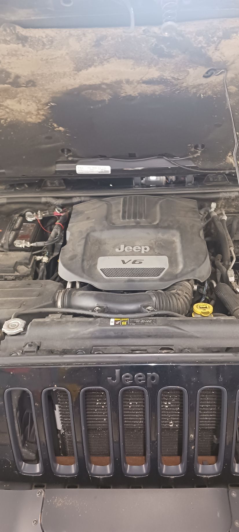Jeep engine bay with hood open, dusty windshield and engine cover visible.