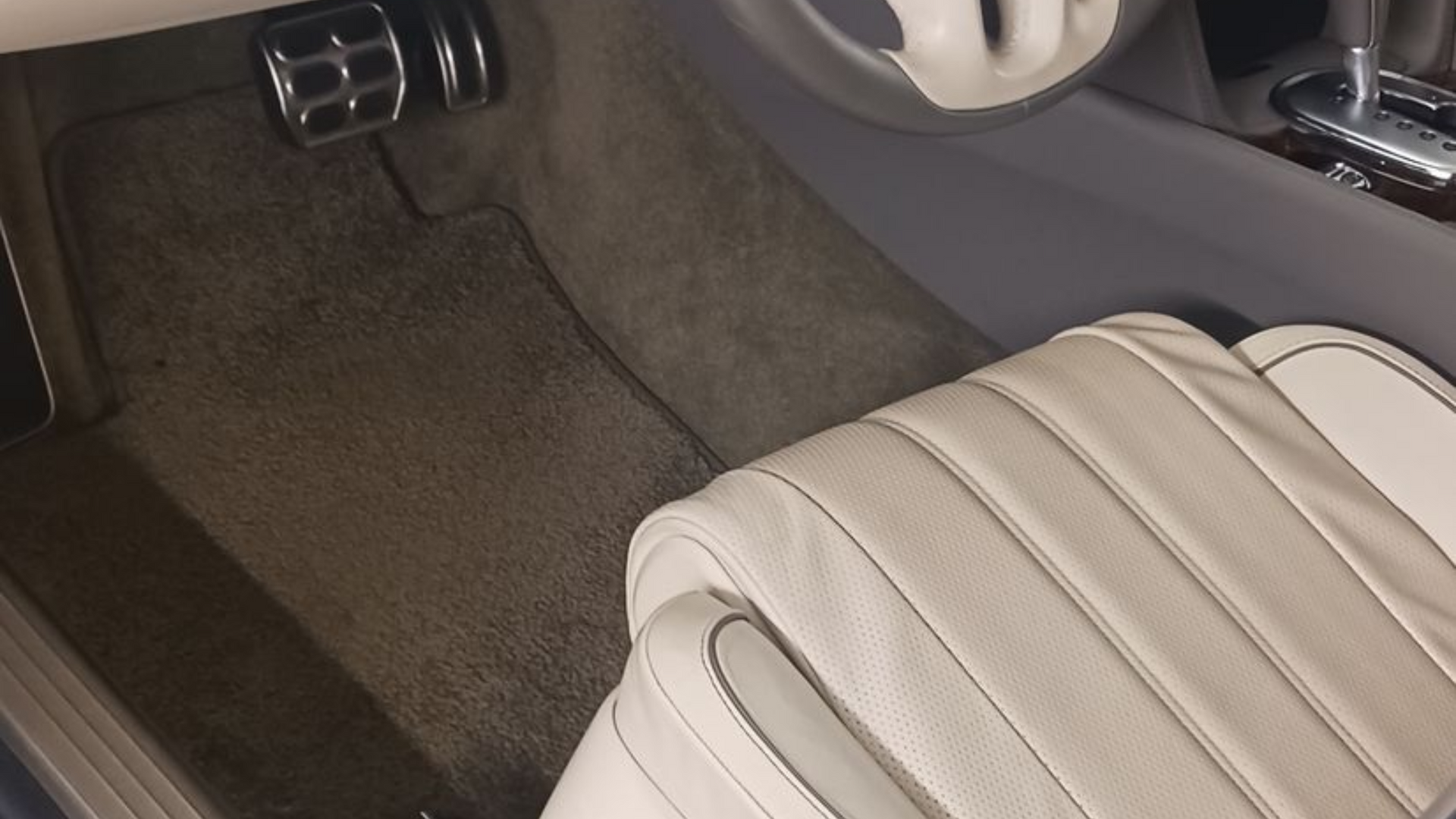 Car interior with beige seat and floor mat near a door panel and air vent