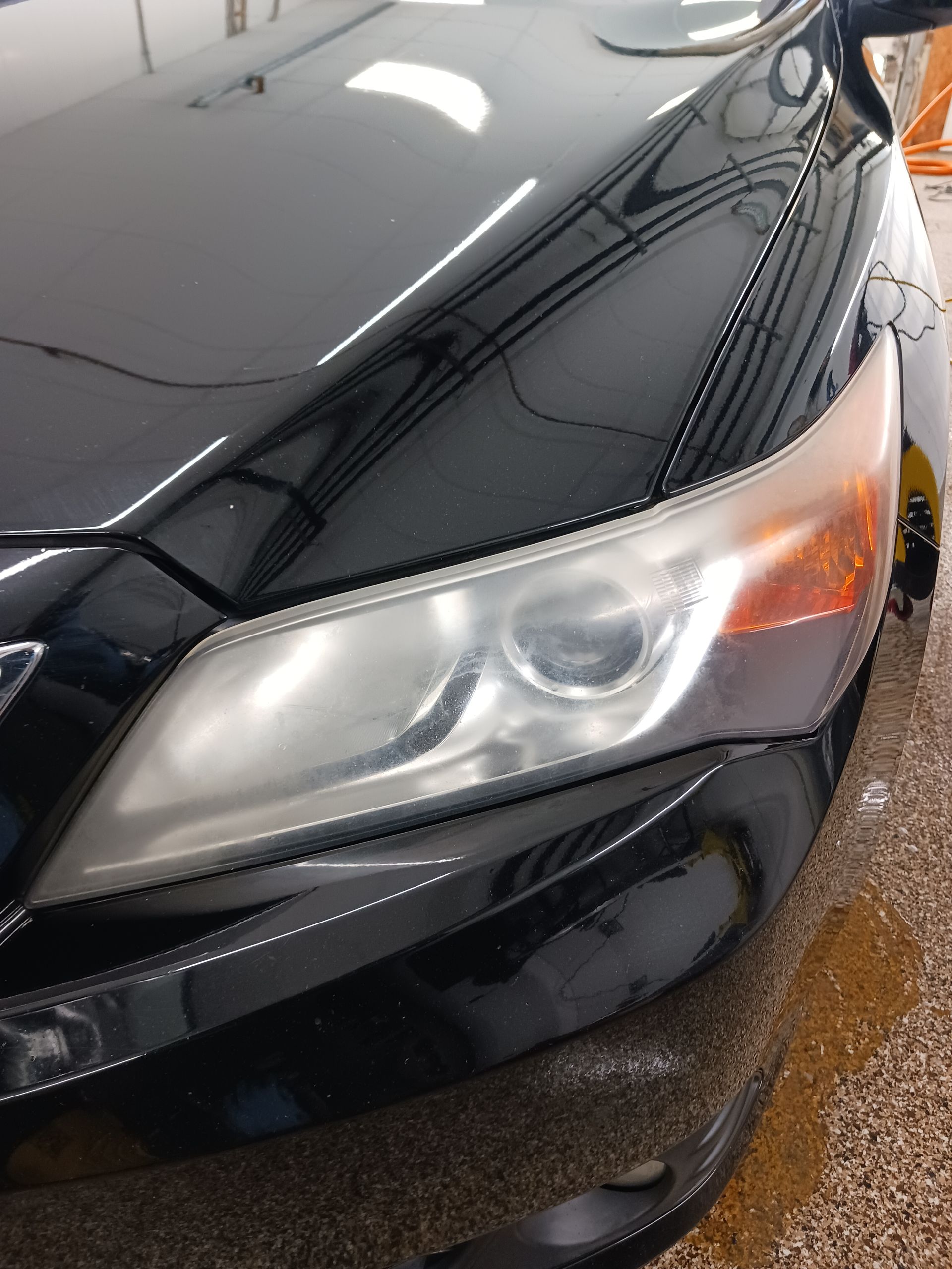 Close-up of a black car’s front headlight and hood in a showroom