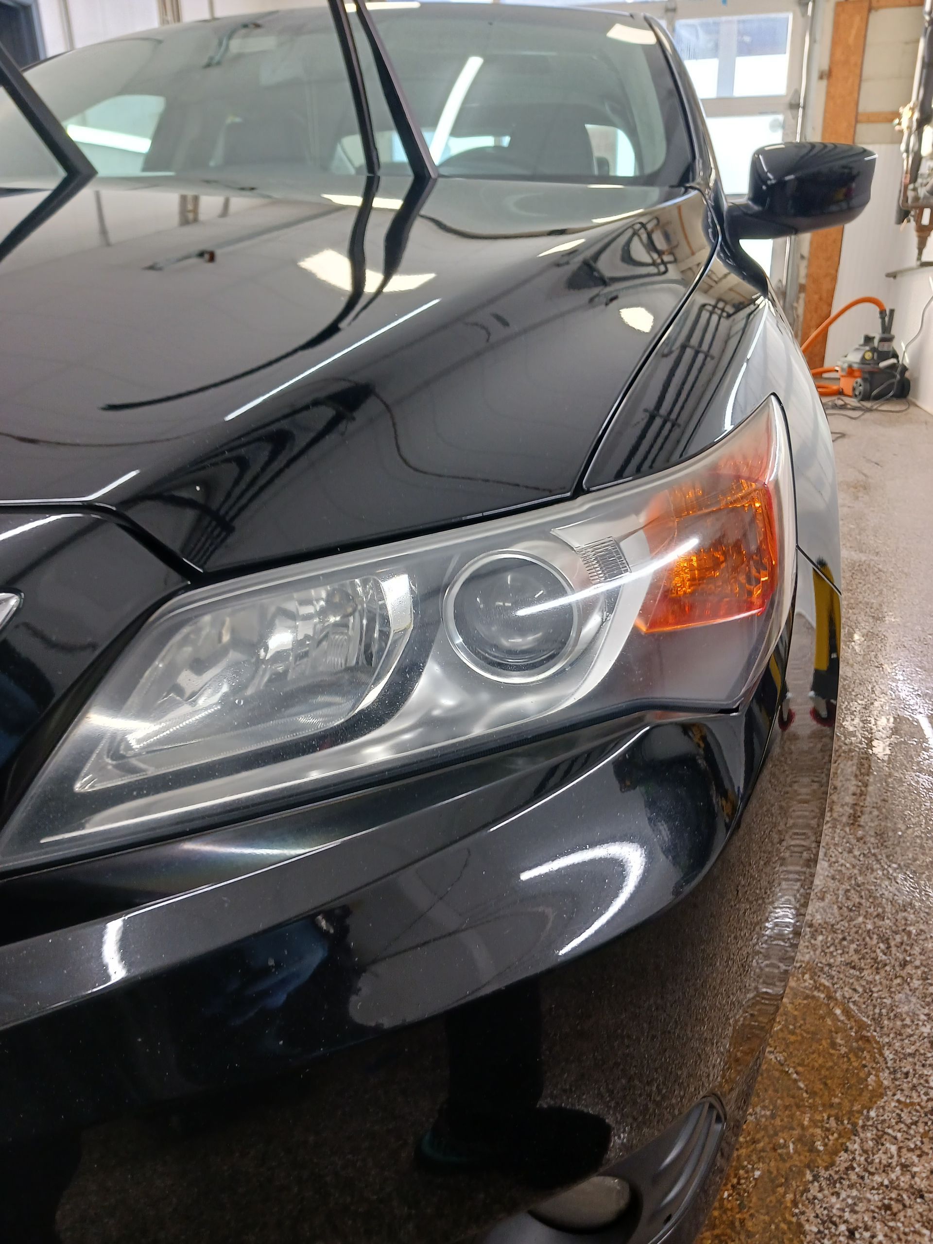 Black car front headlight and bumper in a garage with wet floor