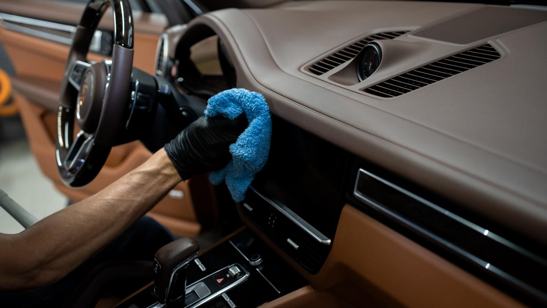 Person wiping a car dashboard with a blue cloth in the front seat area