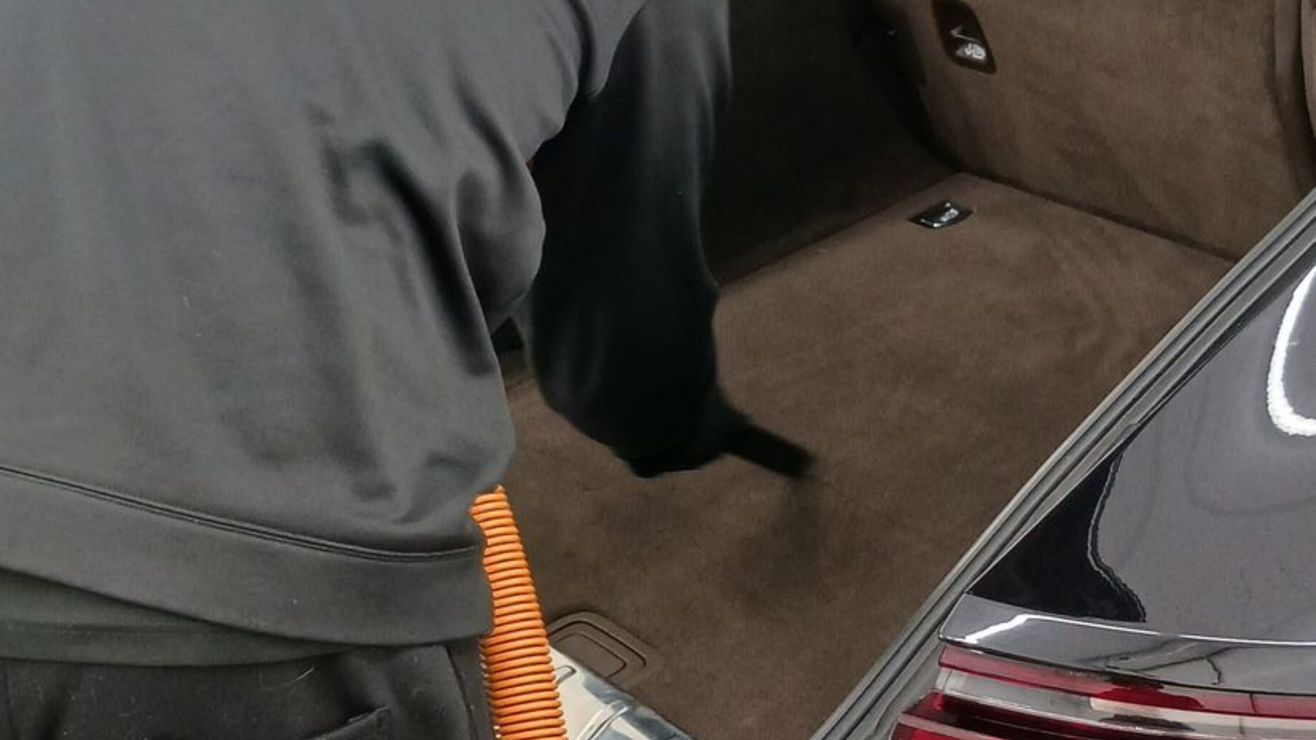 Worker loading equipment into the open trunk of a black car in a garage