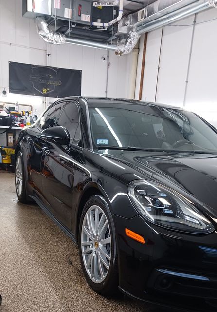 Person polishing a glossy black car with a red buffer in a garage