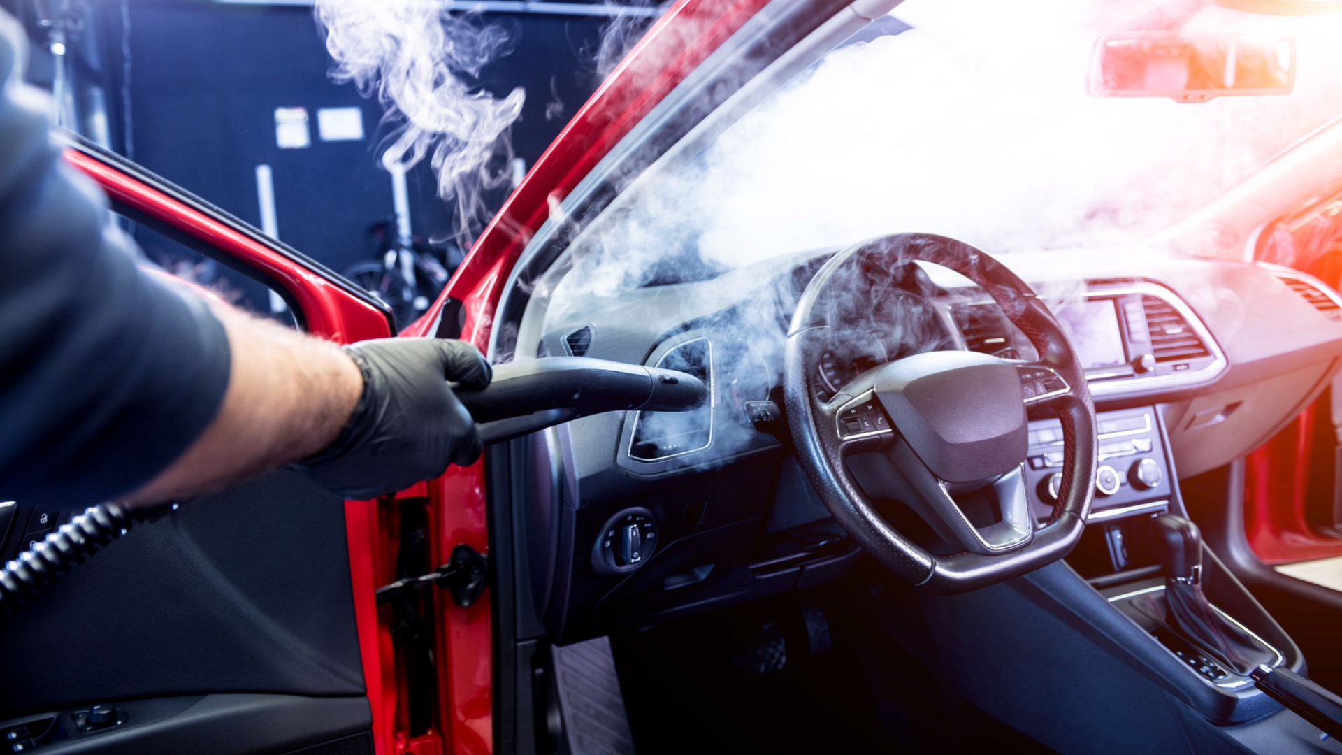 Worker steam-cleans a red car interior, with dashboard and steering wheel visible