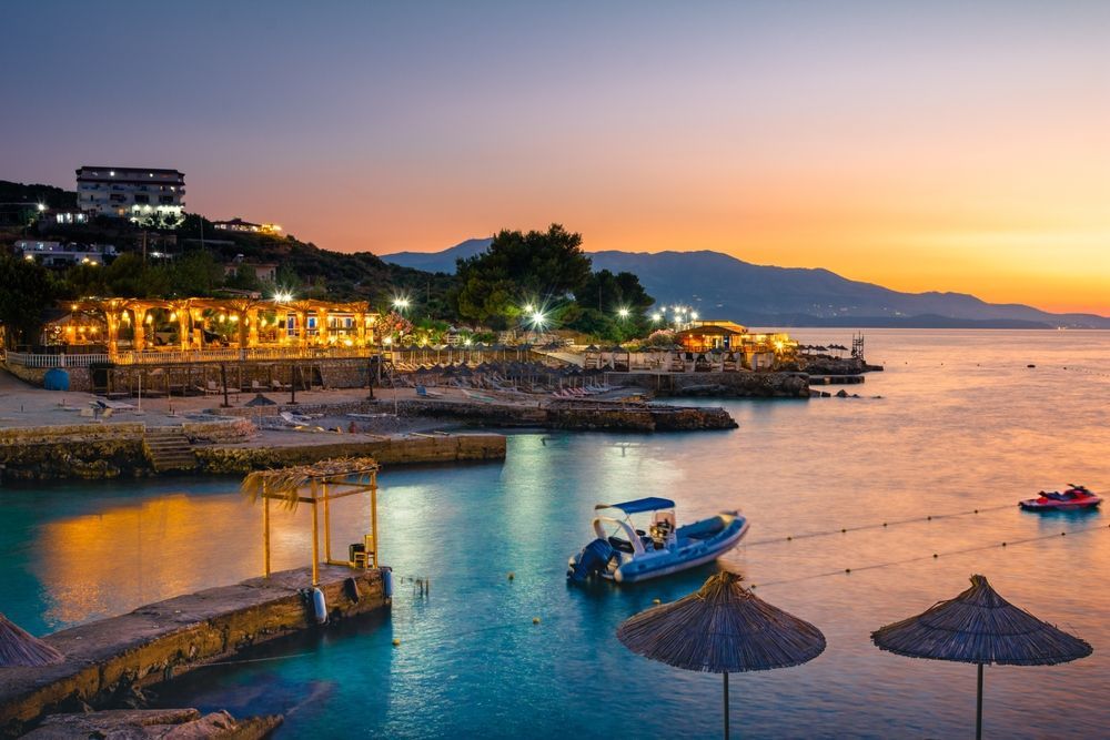 Coastal scene at dusk with illuminated beachside restaurants and boats.