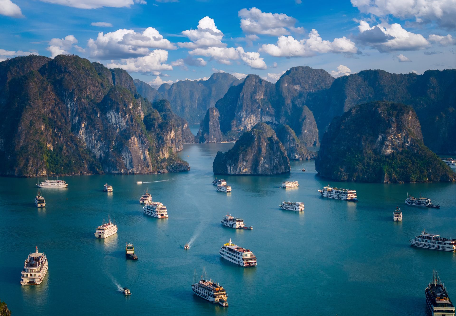 Bay with limestone islands and boats under a partly cloudy sky.