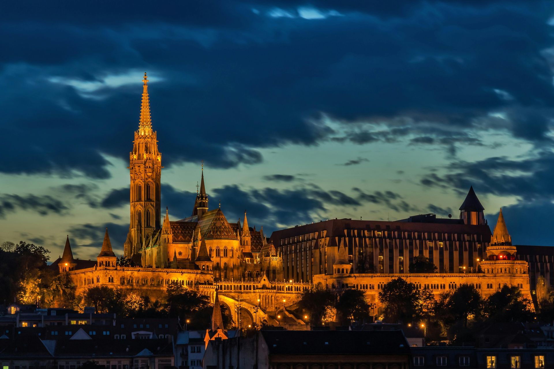 Illuminated Matthias Church and surrounding buildings against a dark blue twilight sky in Budapest.