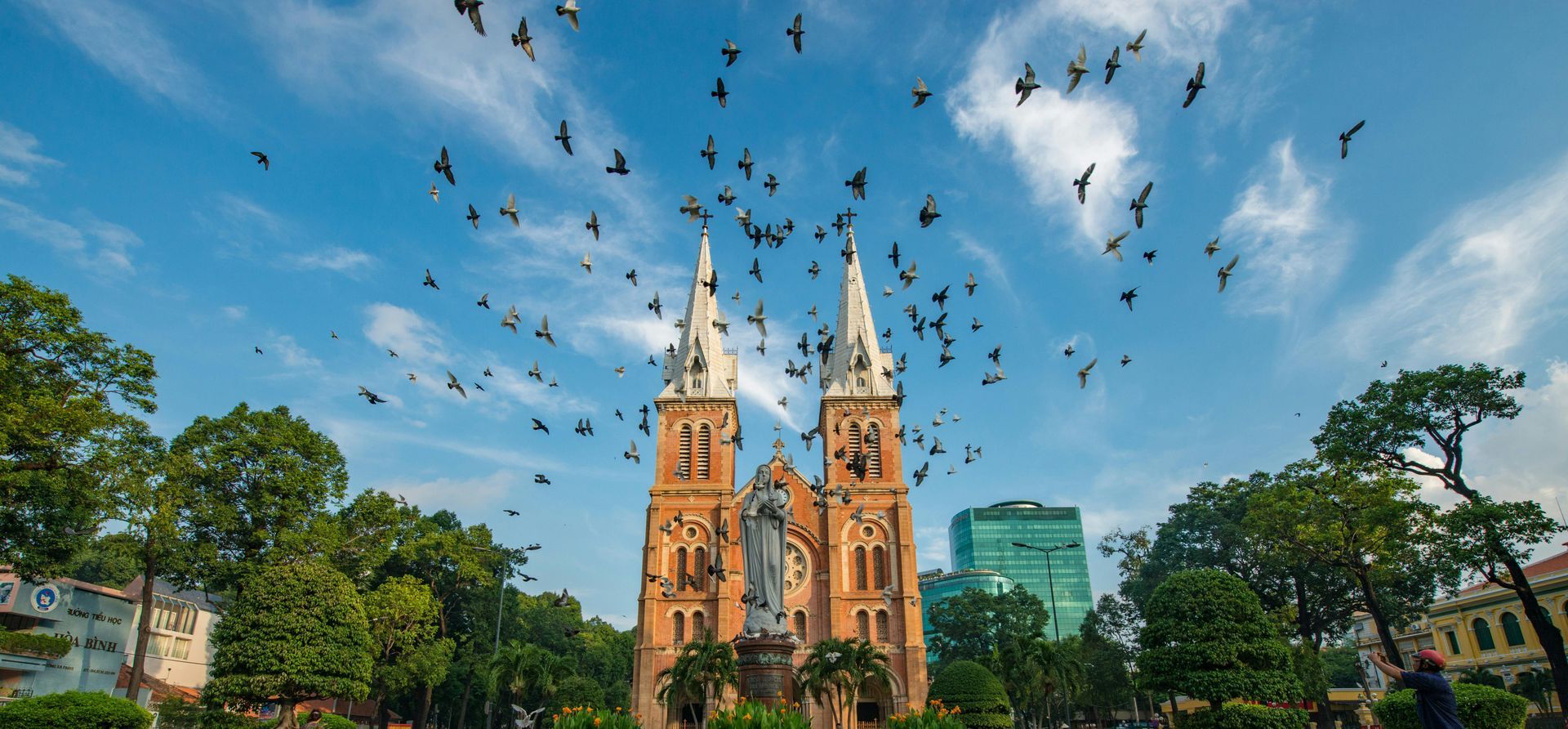 Birds fly over a cathedral with white spires on a sunny day.
