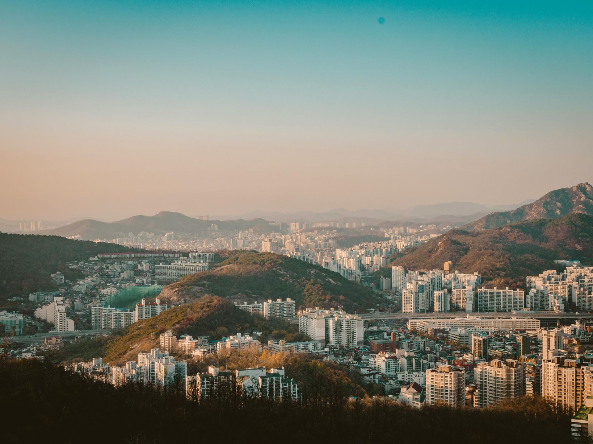 Cityscape with buildings and mountains under a pastel sky.