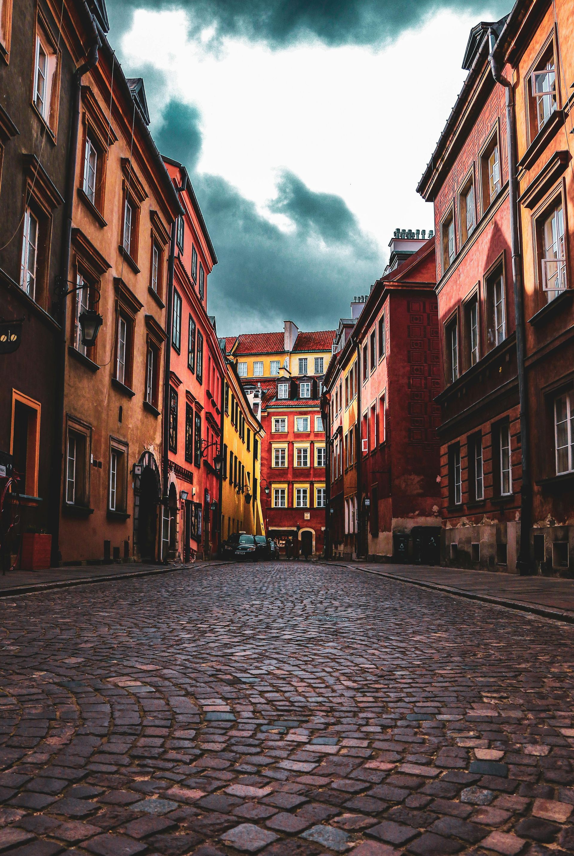 Cobblestone street between colorful buildings under a cloudy sky.