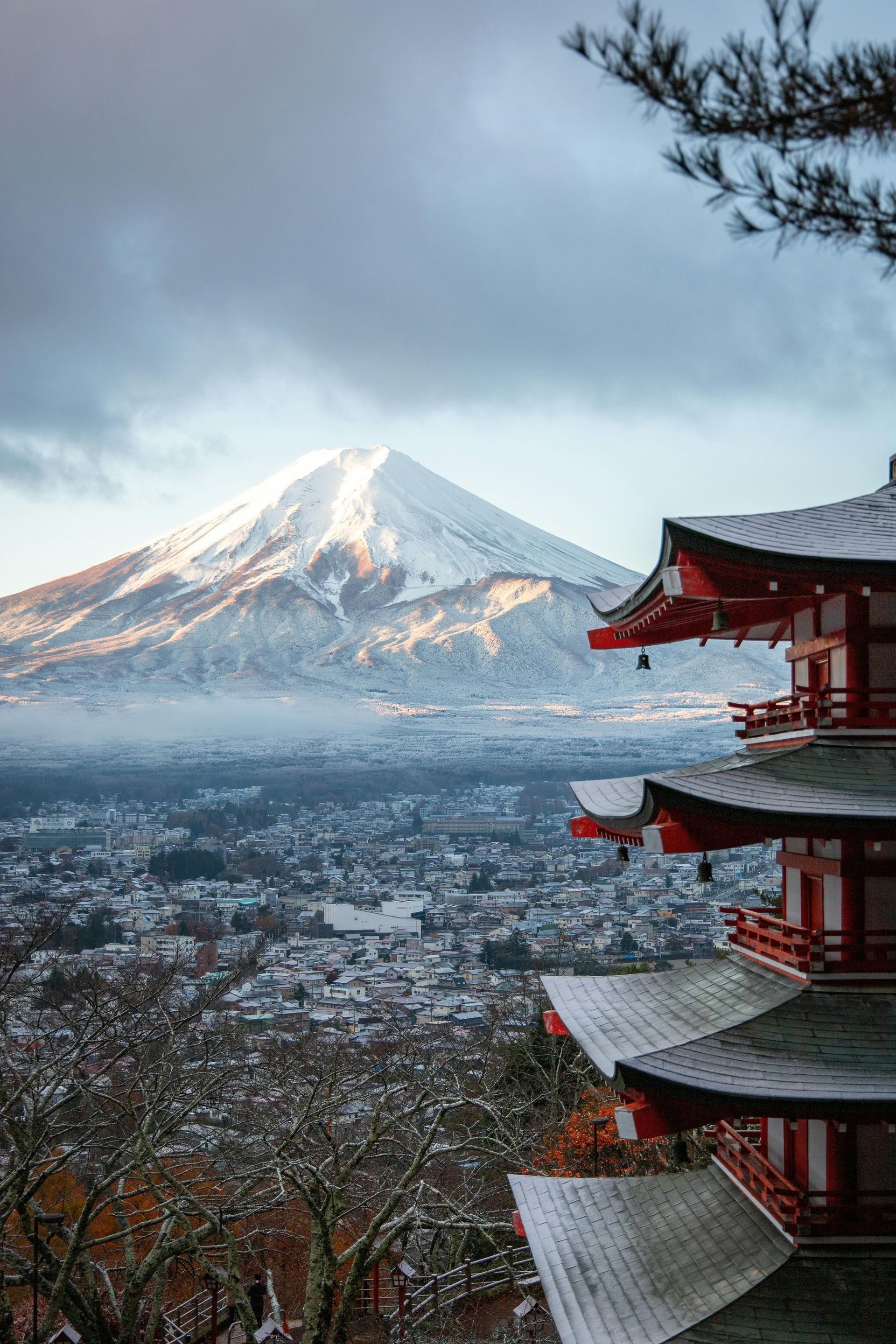 Snow-covered Mount Fuji with a red pagoda in the foreground, overlooking a snowy city.