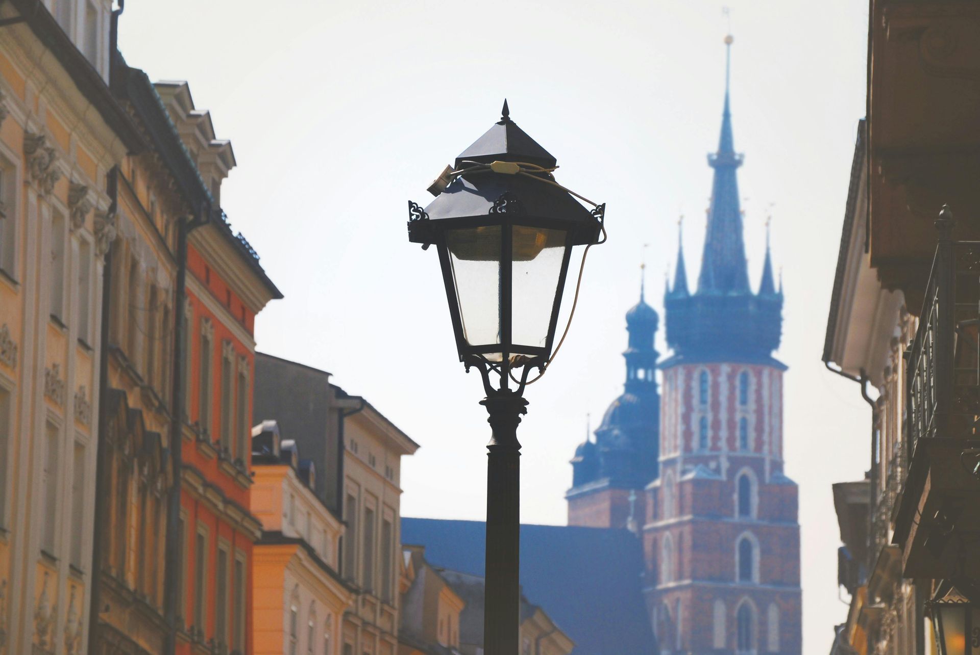 Ornate street lamp in a European city, with a church spire in the background, surrounded by colorful buildings.