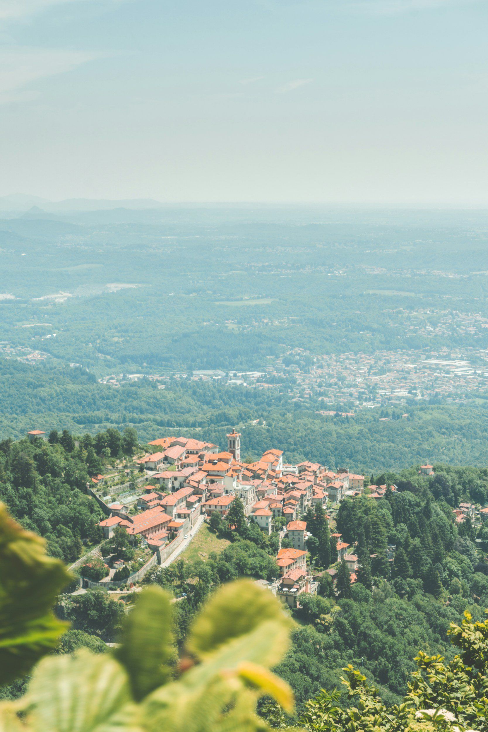 Red-roofed village nestled in green hills, overlooking a vast, forested landscape under a hazy sky.