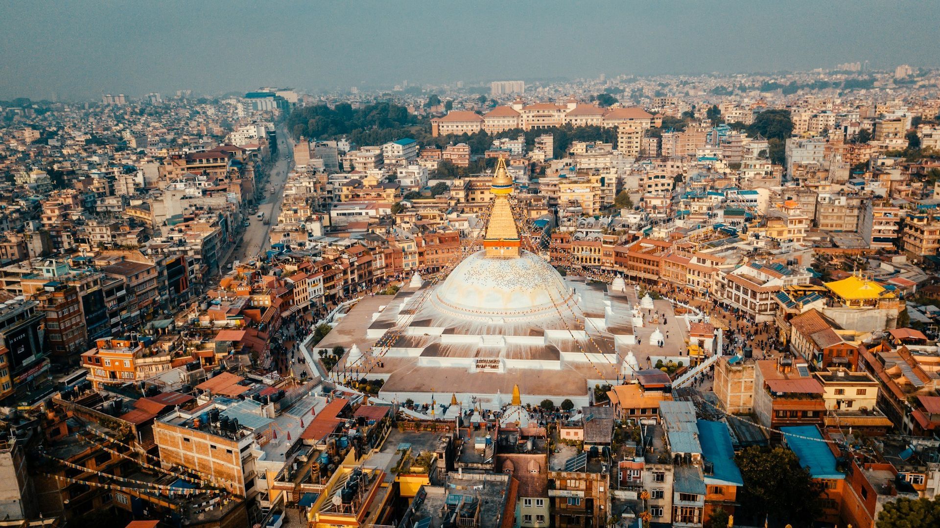Aerial view of Boudhanath Stupa in Kathmandu, Nepal. White stupa surrounded by buildings, a bustling city.