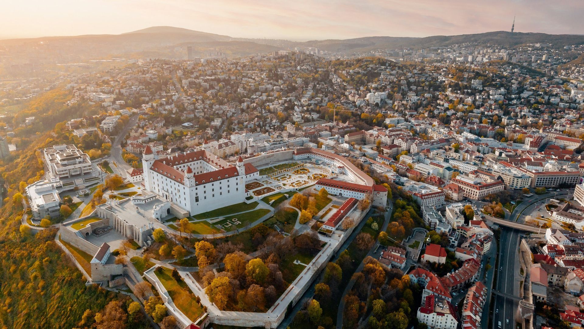 Aerial view of Bratislava Castle and surrounding cityscape in warm light.