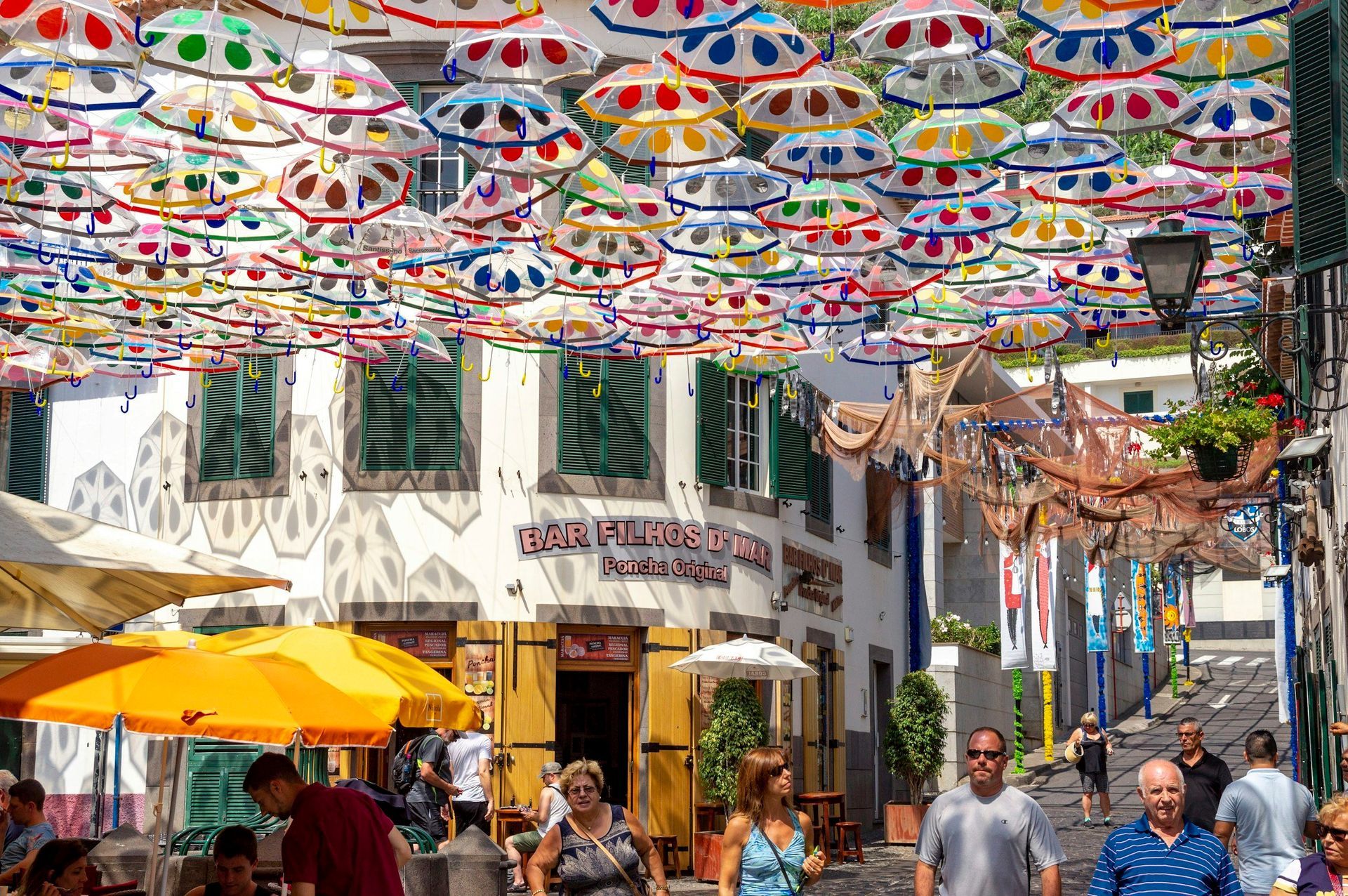 Street scene: Colorful umbrellas shade a pedestrian walkway with shops, restaurants, and people.