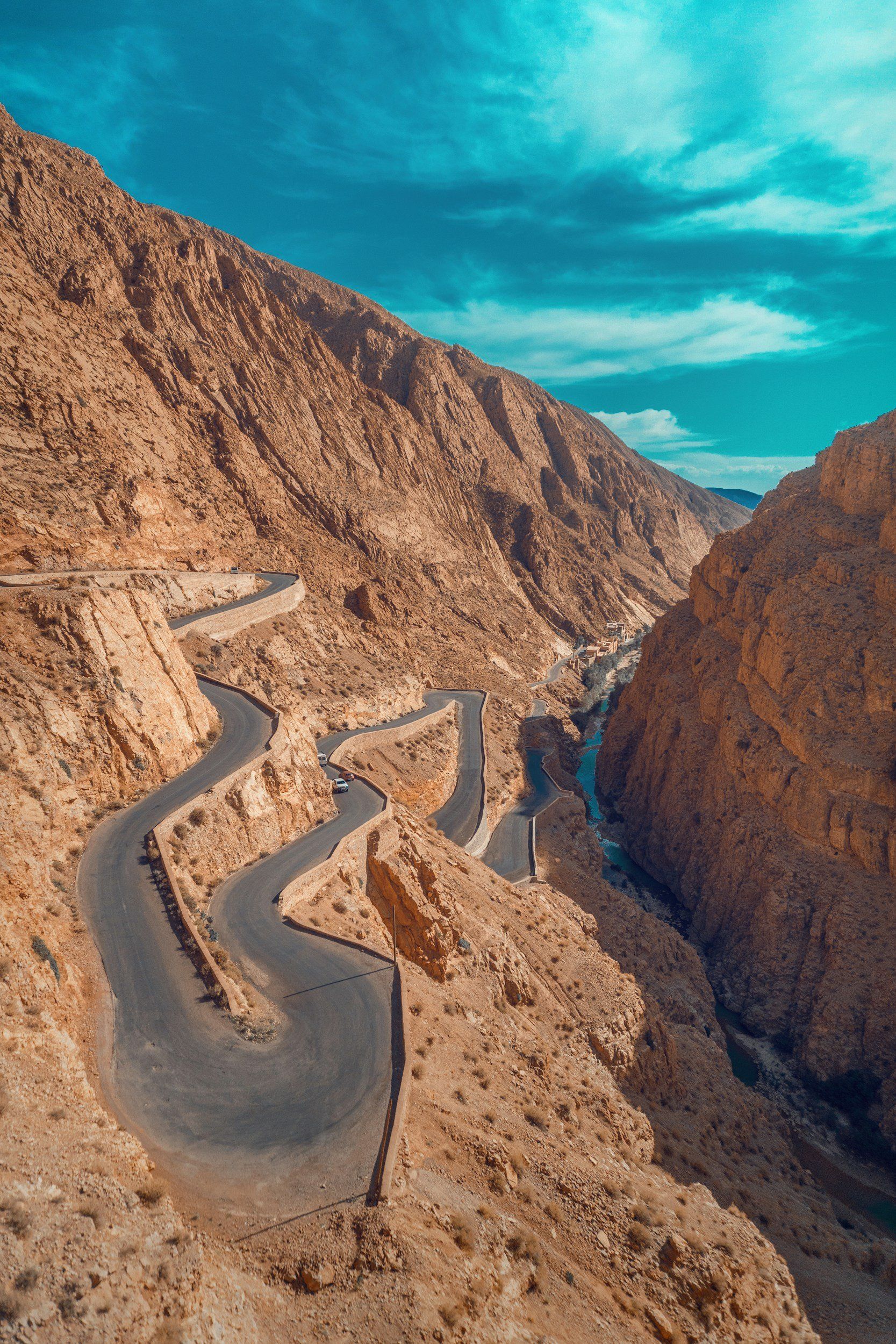 Winding road through a rugged, tan-colored mountain canyon under a blue sky.