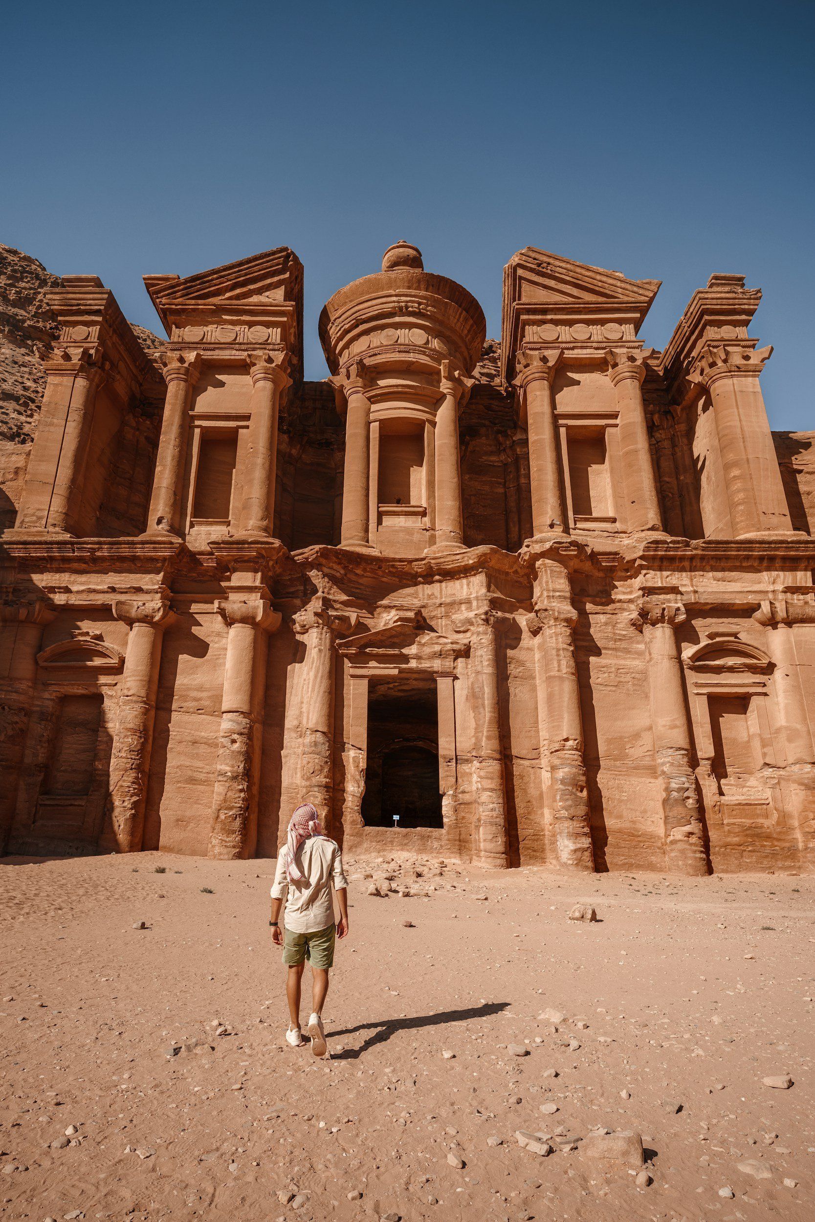 Man walks towards the Monastery, a large, ornate carved sandstone structure, in Petra, Jordan.