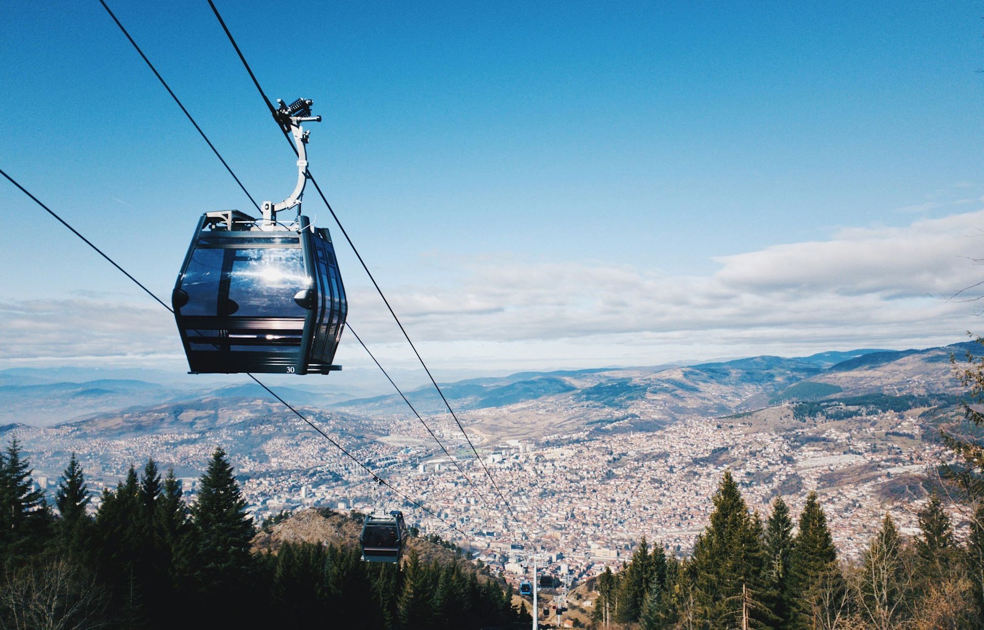 Cable car ascending, overlooking a sprawling city under a clear blue sky.