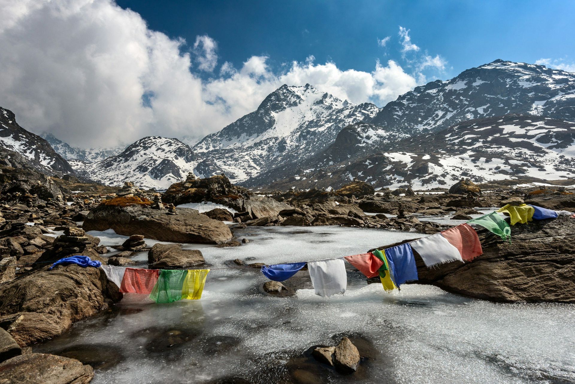 Snowy mountain landscape with prayer flags strung over a partially frozen river.
