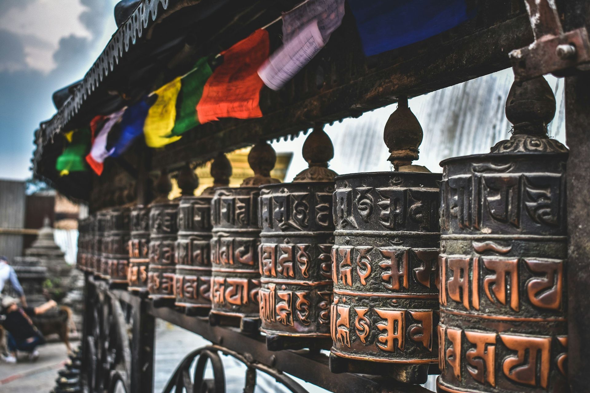 Prayer wheels with colorful prayer flags in a row, likely in a temple in Nepal.