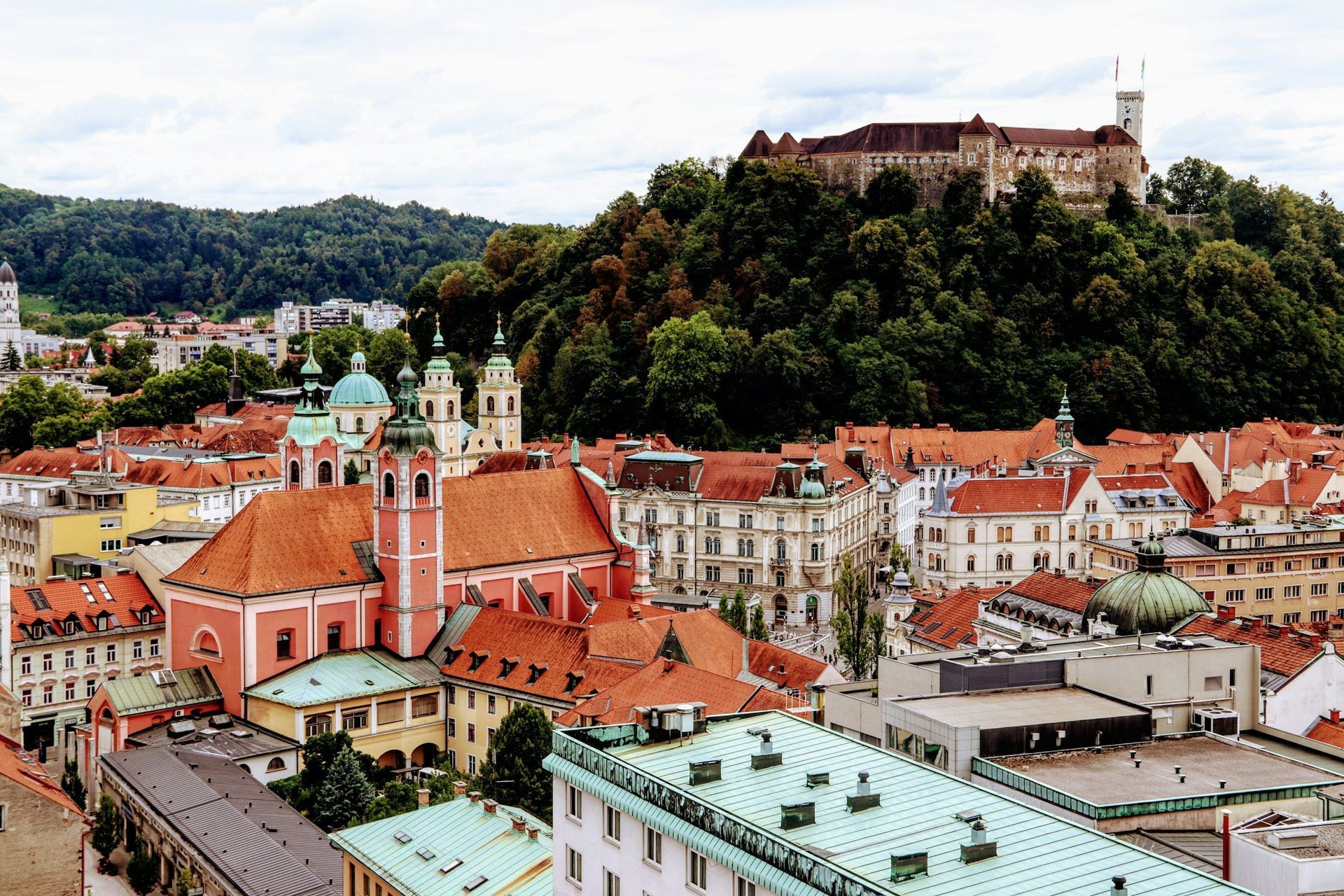 Ljubljana, Slovenia cityscape with red-tiled roofs, a church with green domes, and Ljubljana Castle on a hill.