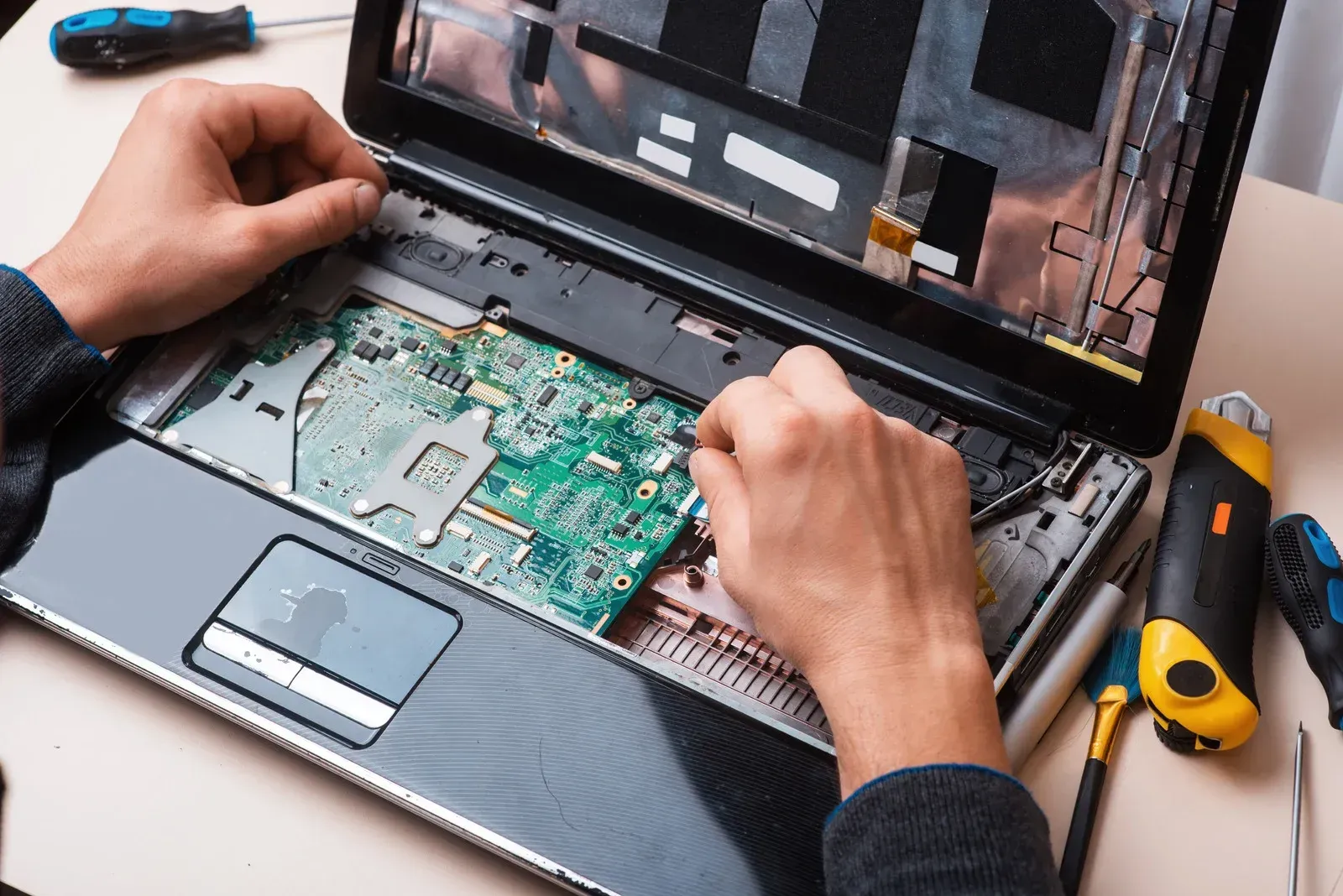 A person is repairing a laptop computer with tools on a table.