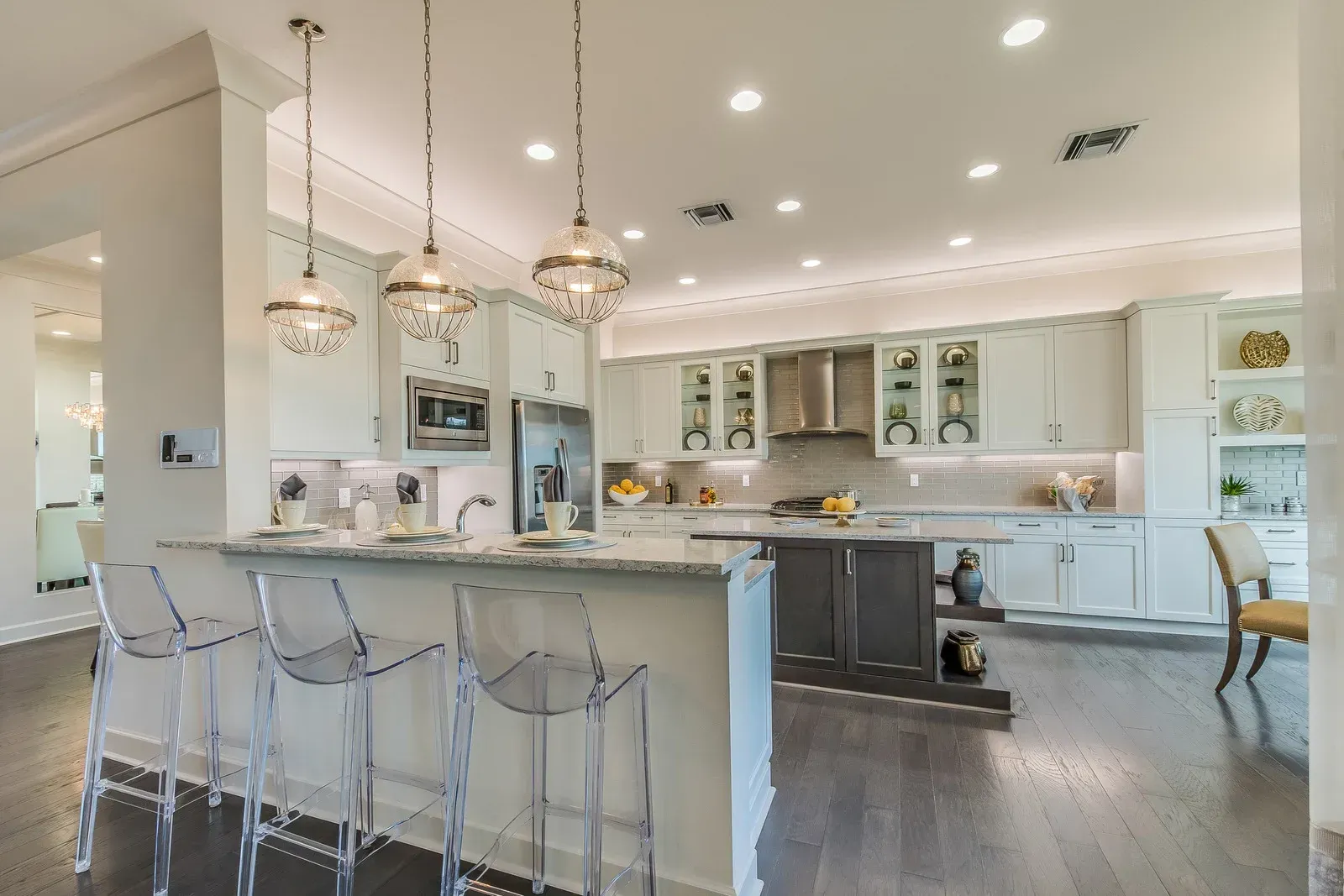 A kitchen with white cabinets , stainless steel appliances , a large island , and clear bar stools.