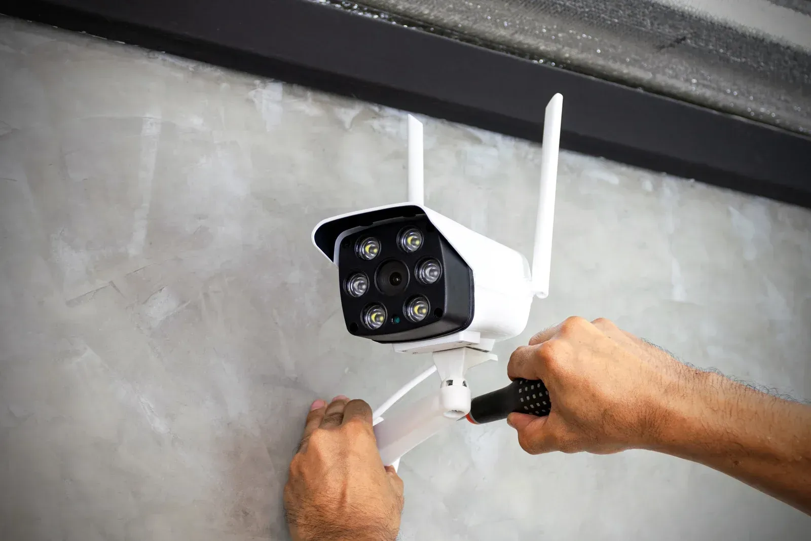 A person is installing a security camera on a wall.