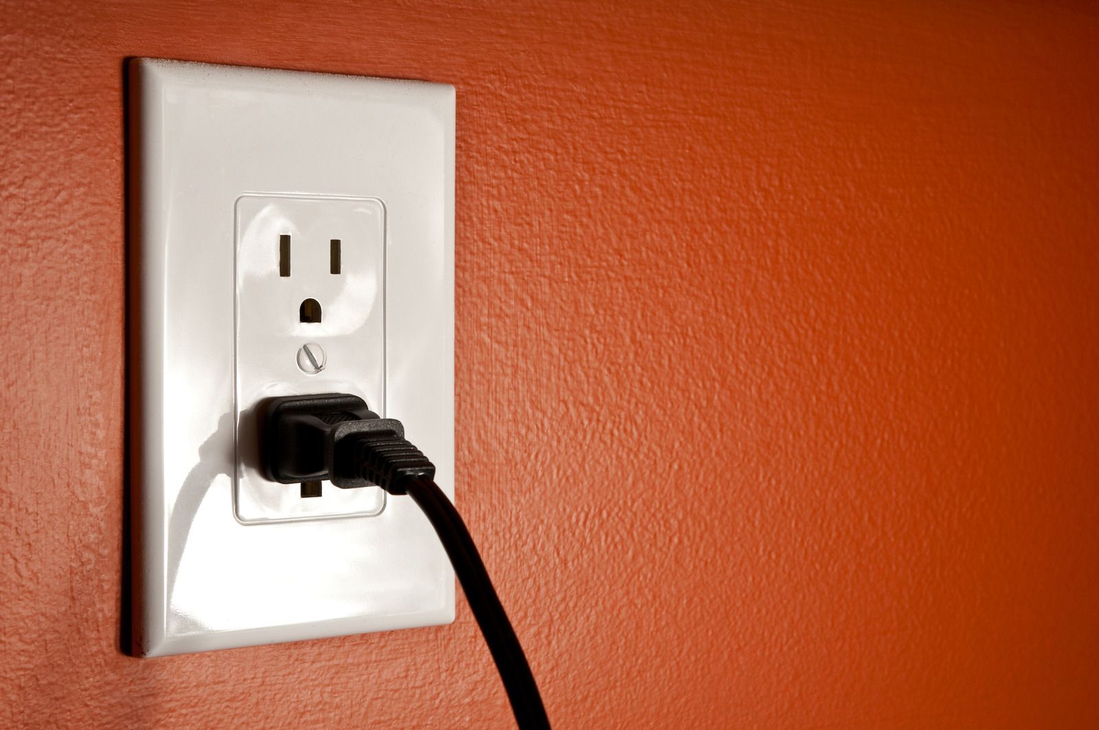 A black cord is plugged into an electrical outlet on an orange wall.