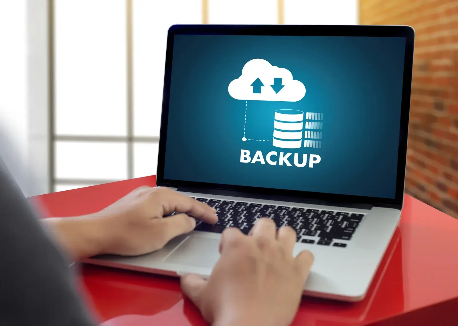 A person is typing on a laptop with the word backup on the screen.