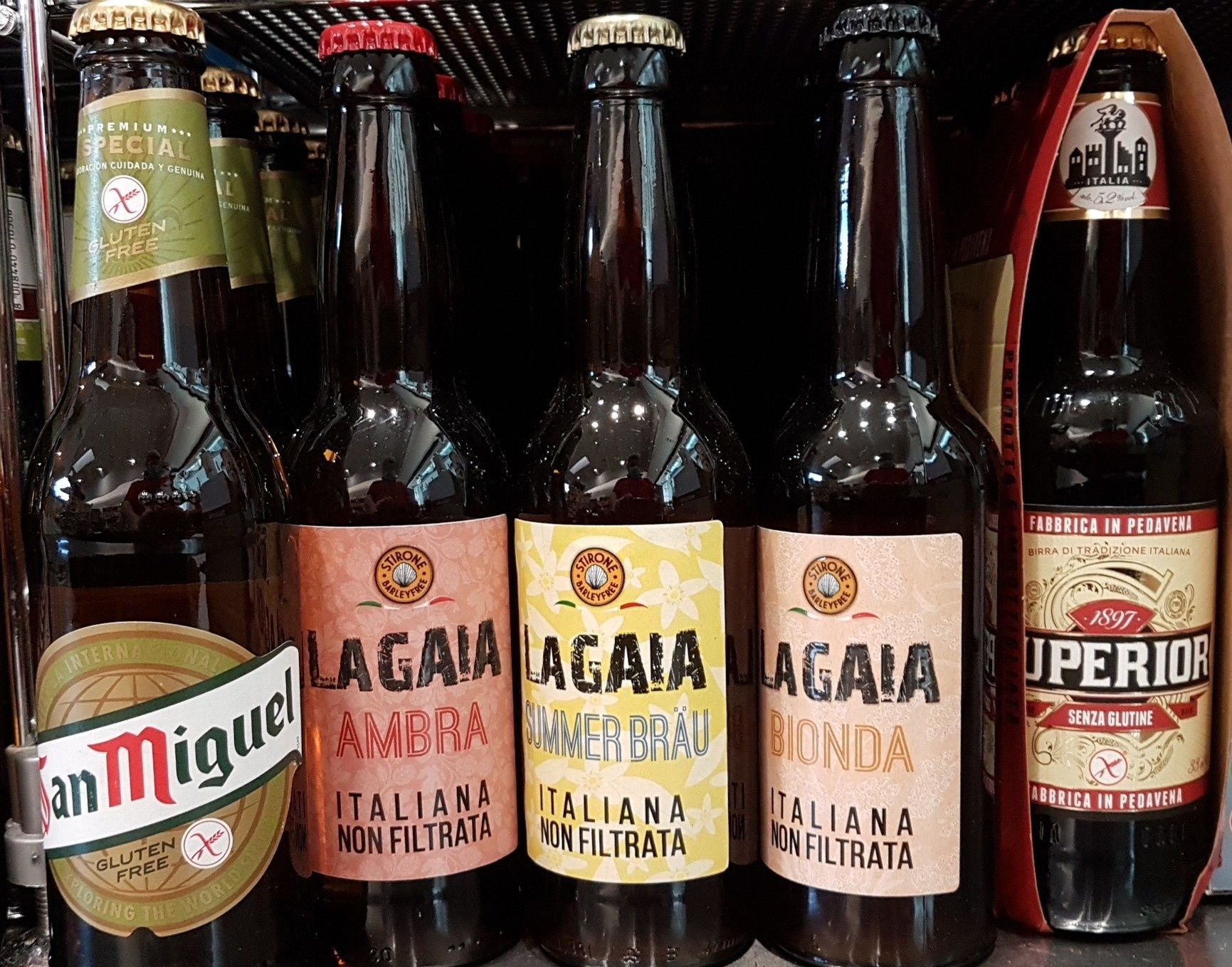 Bottiglie di birra italiana su uno scaffale, tra cui San Miguel, Lagaia Ambra e Lagaia Bionda.