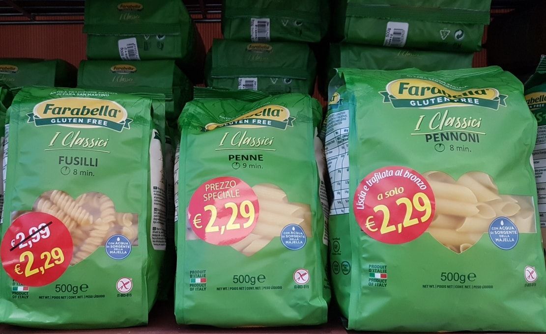 Tre sacchetti verdi di pasta con etichette rosse del prezzo sullo scaffale di un negozio.