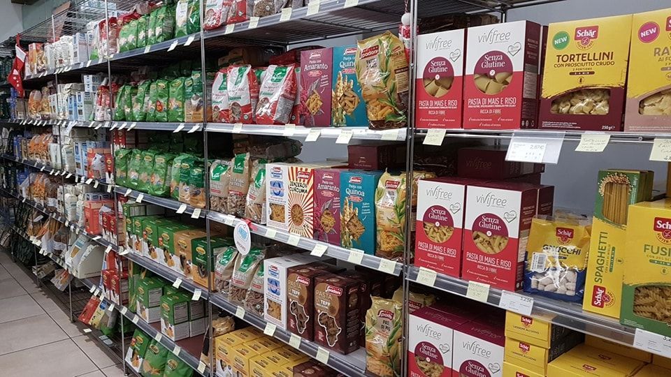 Scaffali pieni di vari prodotti alimentari confezionati nel corridoio di un supermercato.