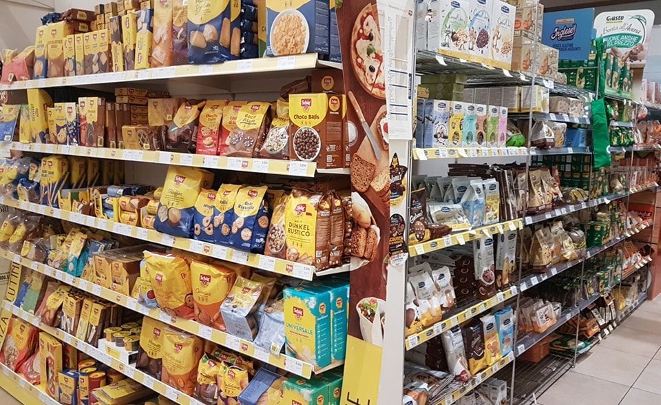 Scaffali pieni di vari prodotti alimentari confezionati nel corridoio di un supermercato.